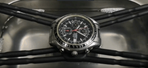 A luxury wristwatch with a metal band mounted on a stand inside an ultrasonic cleaner